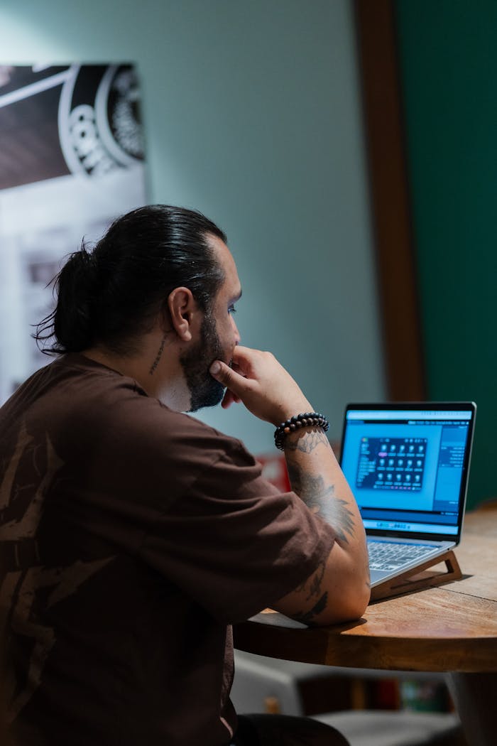 Man seated at a cafe table working on a laptop, focused on his screen.